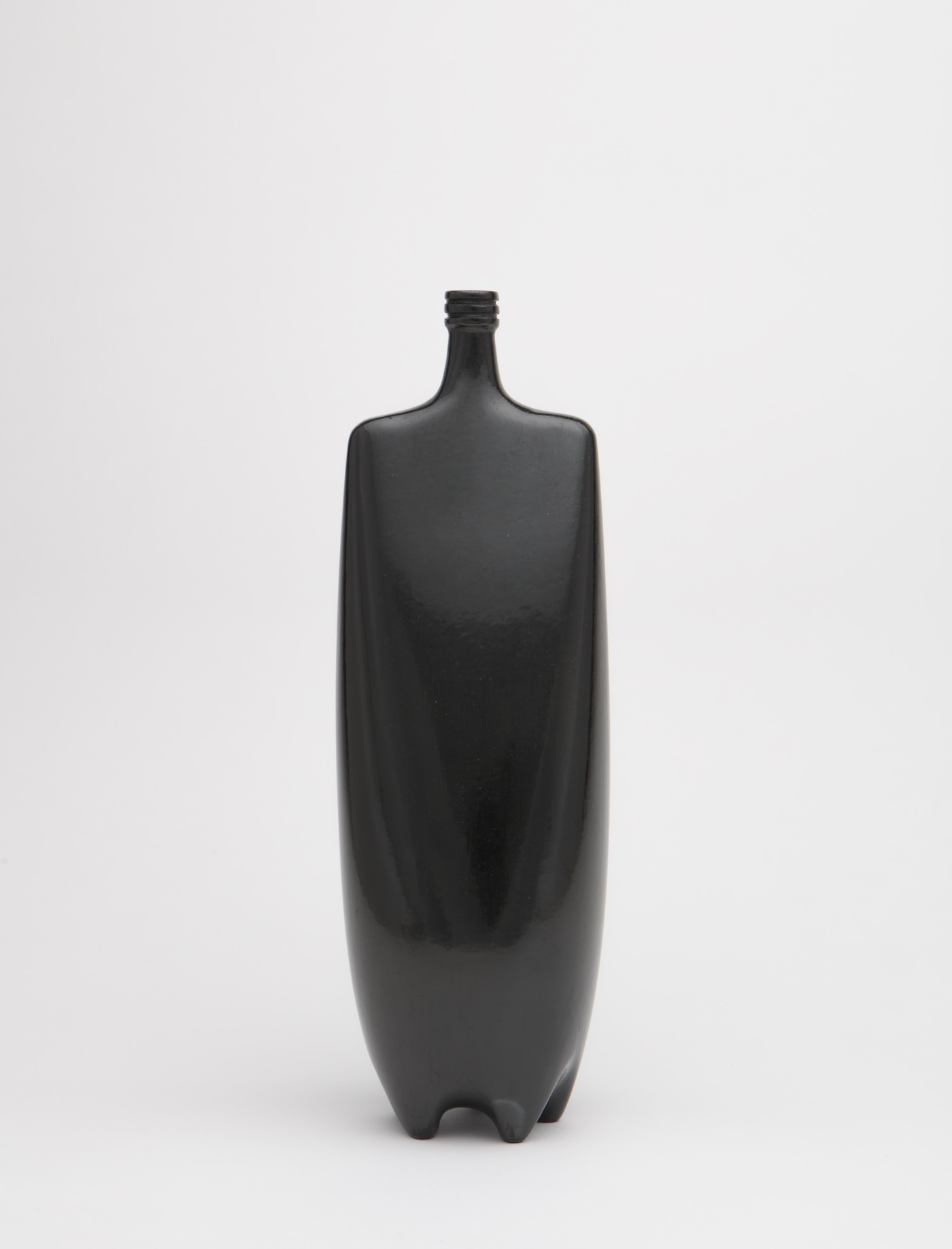 Shiny, black sculpture made of clay resembles a bottle with a square top and rounded body.