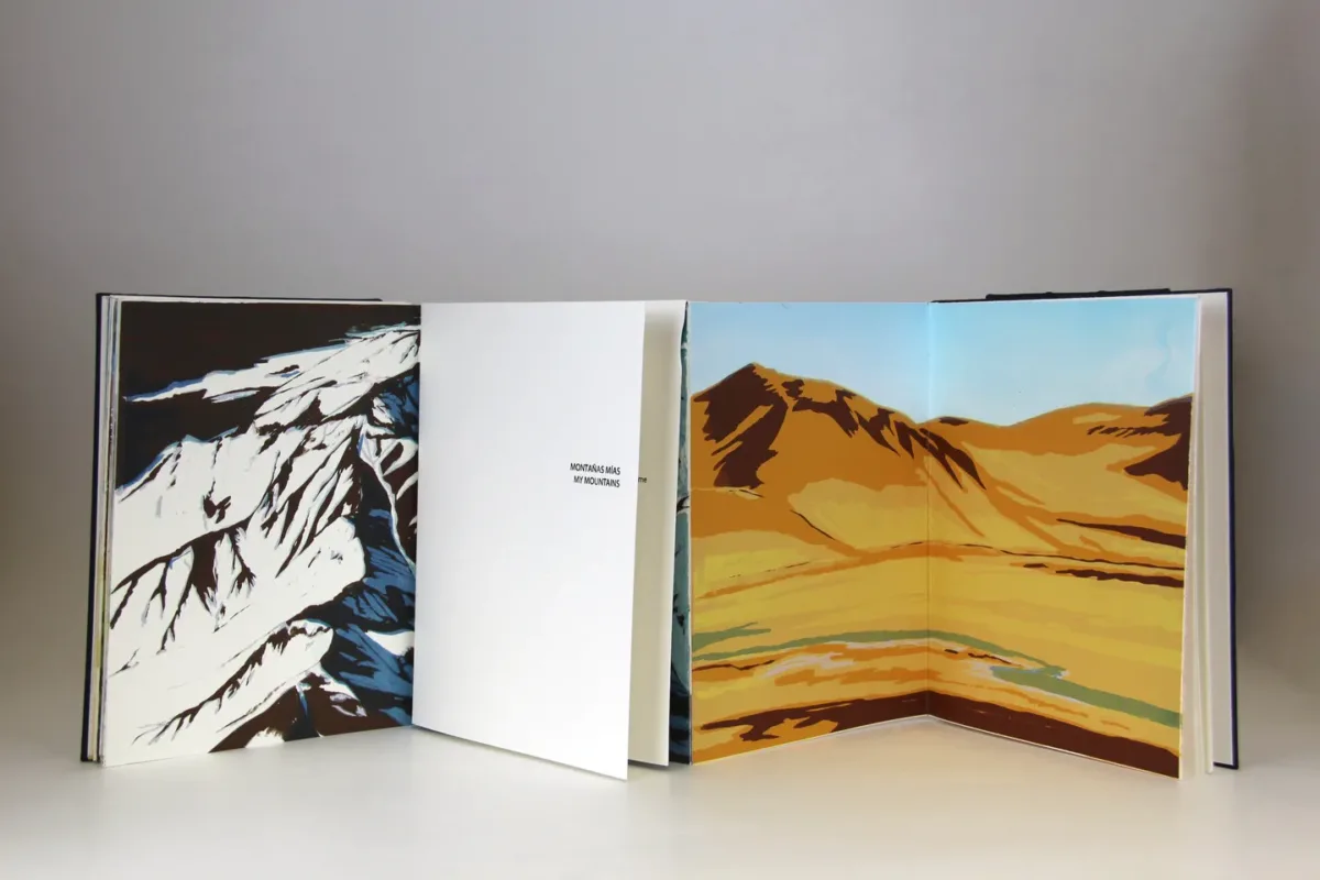 Four leaves of an open book depict mountain ranges. One image shows snow-capped mountains in blue, black and white; the other image depicts a low mountain in desert colors of beige, brown and yellow with a stream in the foreground.