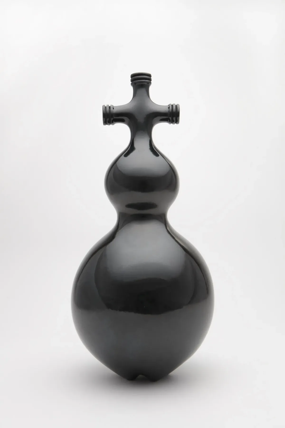 Black, shiny sculpture made of clay features a cross-like shape on top of two bulbs of increasing size.