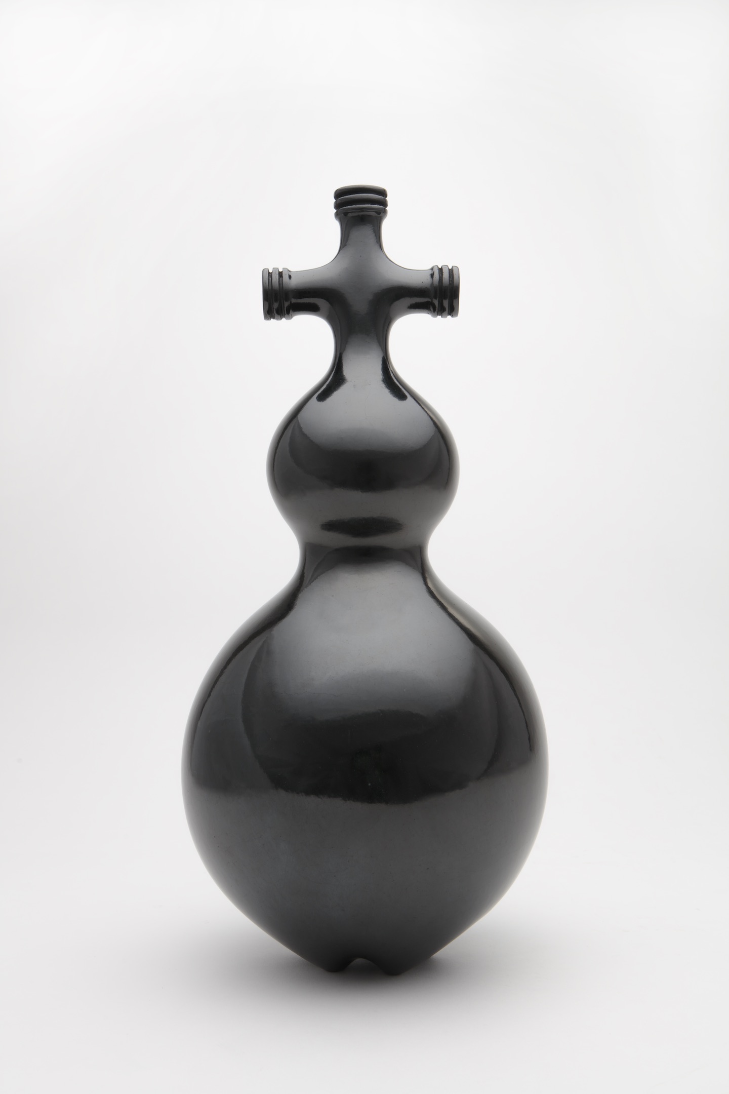 Black, shiny sculpture made of clay features a cross-like shape on top of two bulbs of increasing size.