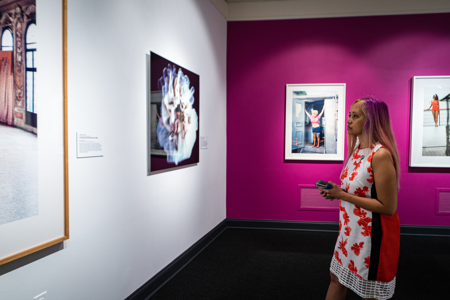 A women stands facing a white wall with two artworks. On the adjacent wall are two more artworks against a bright pink backdrop.