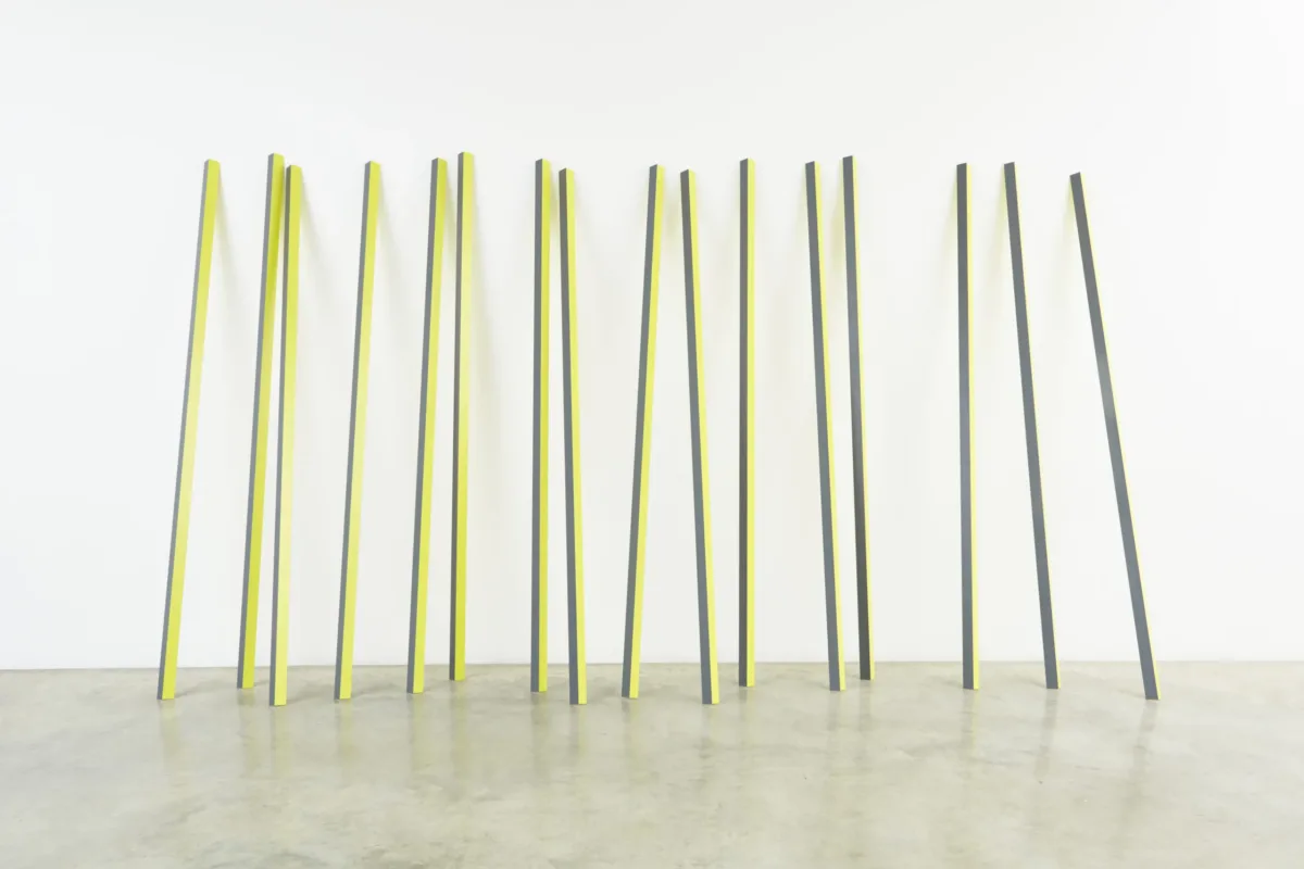 Sixteen rectangular yellow and grey aluminum poles lean up against a wall