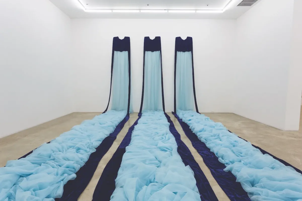 Three long fabric trains in two shades of blue, mounted on a far wall and cascading onto the floor like a waterfall.