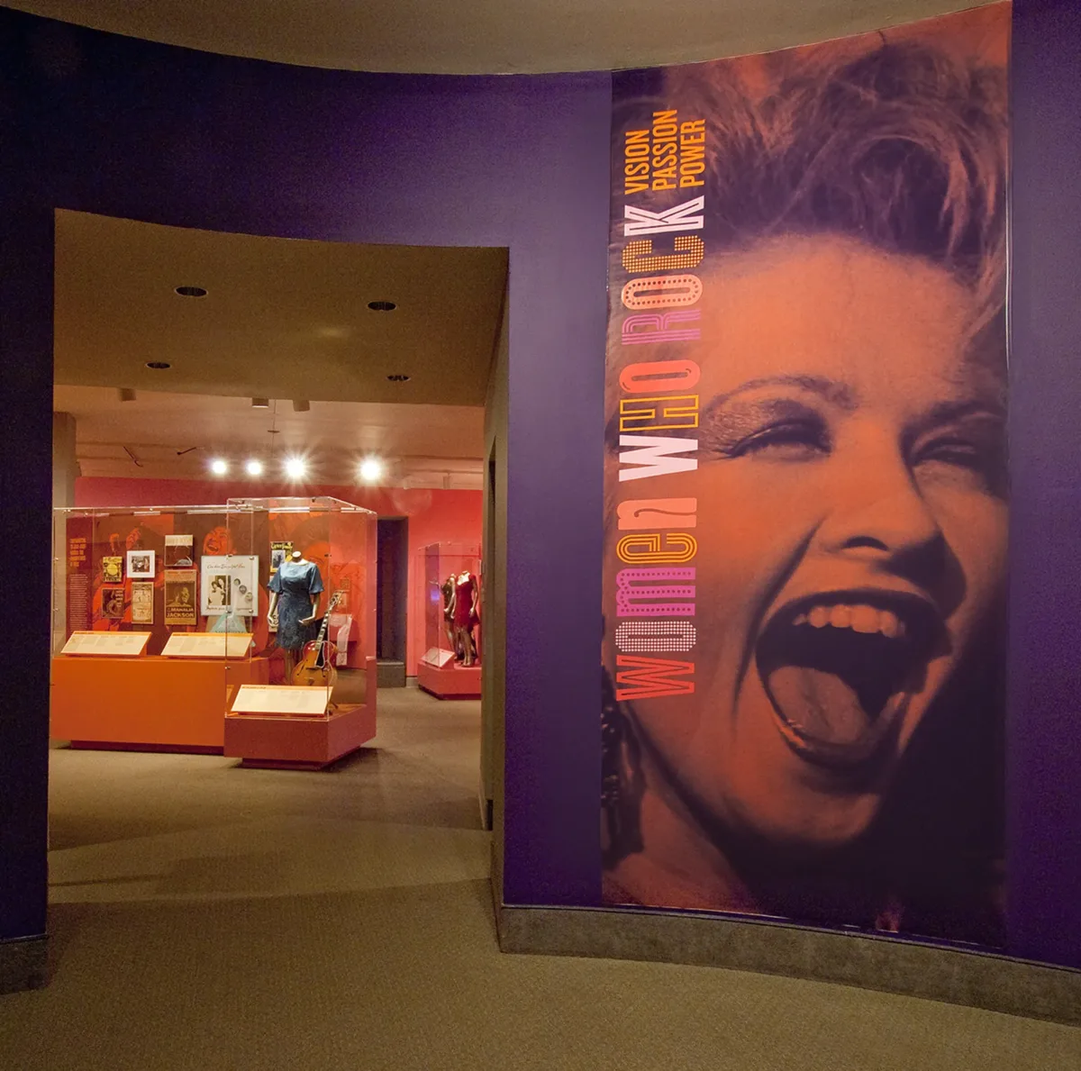 Gallery view showing a purple wall with a photo mural of Debbie Harry singing and the title of the exhibition: Women Who Rock