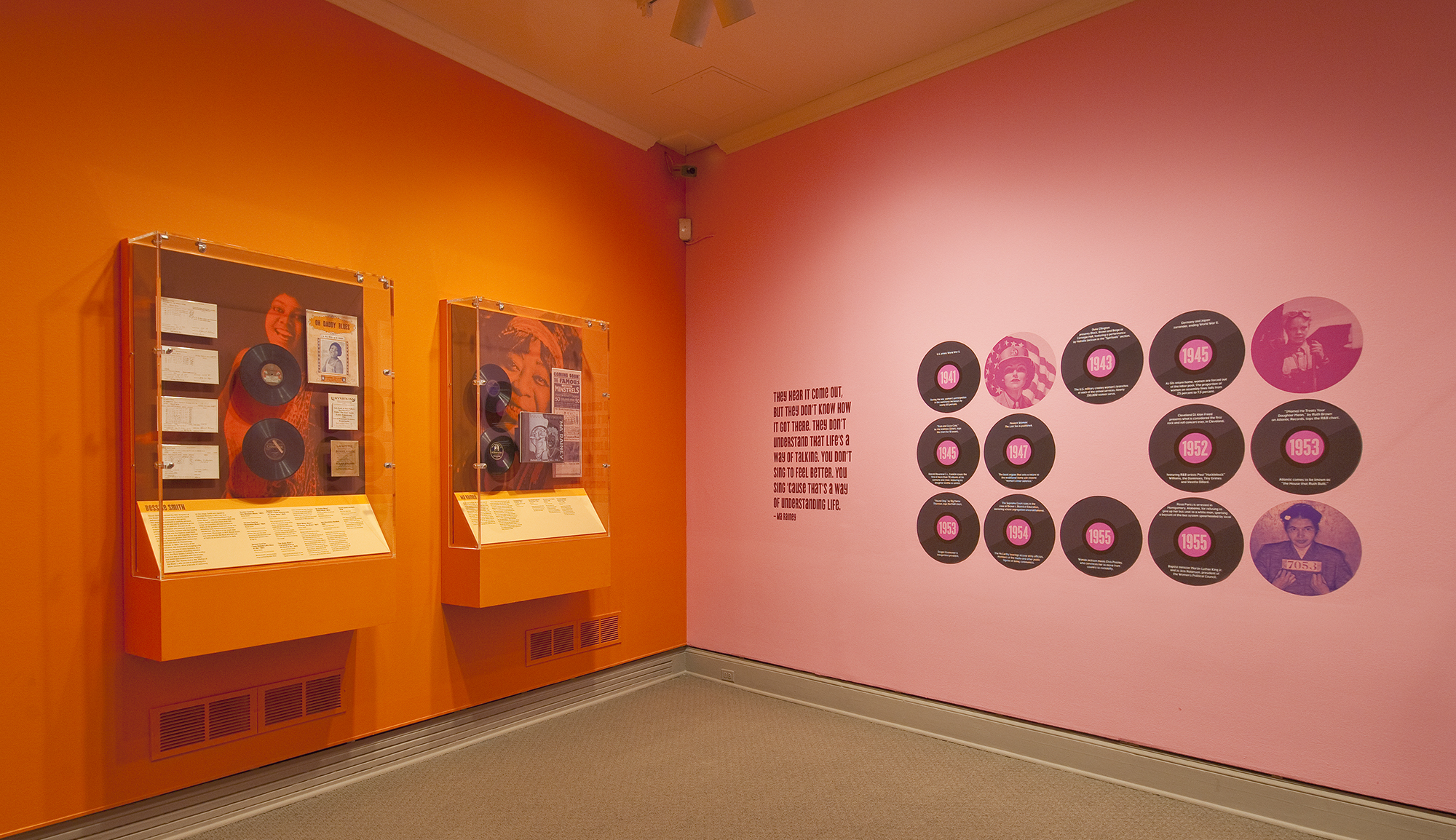 Gallery view showing an orange wall meeting a pink wall and records mounted on each.