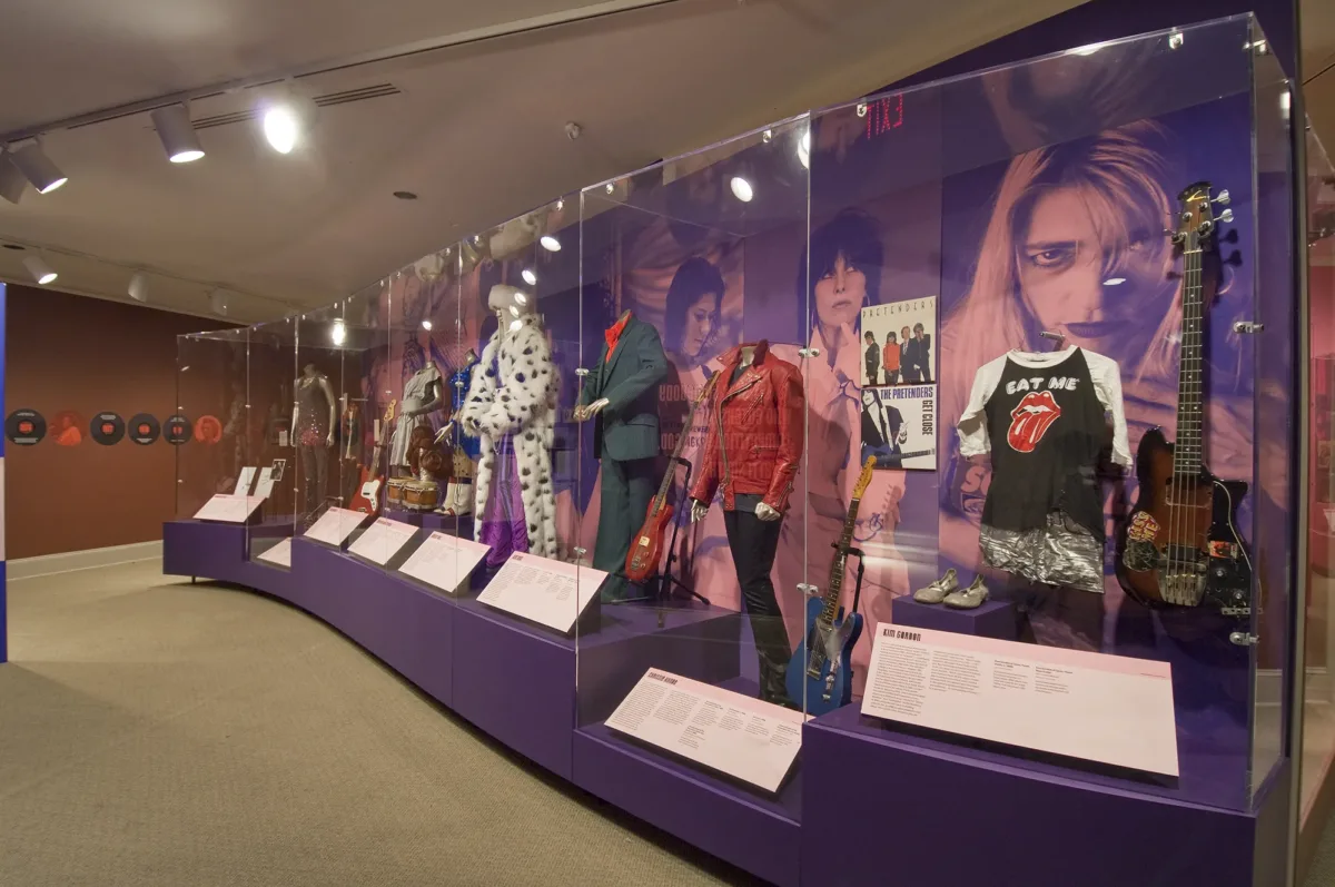 Gallery view showing a display case full of costumes and photo murals of women singers in the background.