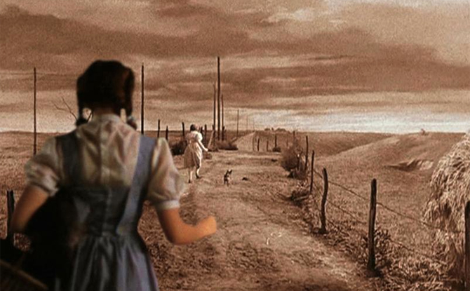 Surrealist film still depicting Dorothy from the Wizard of Oz. In black and white, the scene is Dorothy running away from the viewer along a road wih her dog, Toto. In the forground, the same Dorothy, but in technicolor, chases after her.