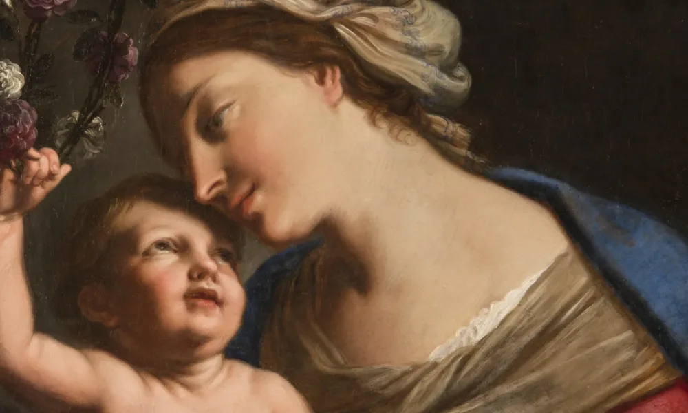 A young, light-skinned, brunette woman gazes down lovingly at the plump baby she holds on her lap. She wears a loose, tan turban, vivid blue cloak, and red dress with white sleeves. The light-skinned child returns her gaze, leaning back to crown the woman with a circlet of roses.