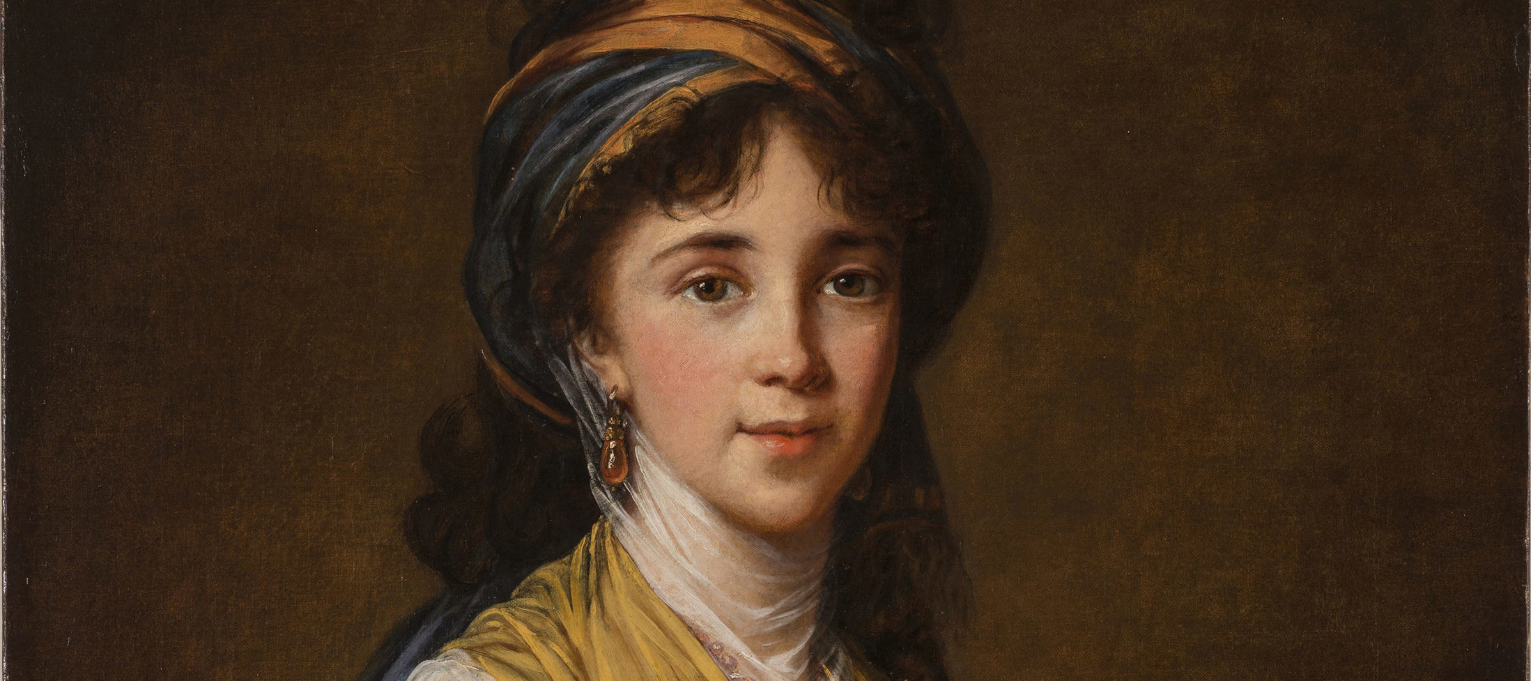 Realistically rendered half-portrait of a light-skinned young woman, gazing directly at the viewer with a faint smile on her lips. Her dark, curly hair is attractively tousled, secured under a turban-like headdress which matches her gold and blue draped ensemble.
