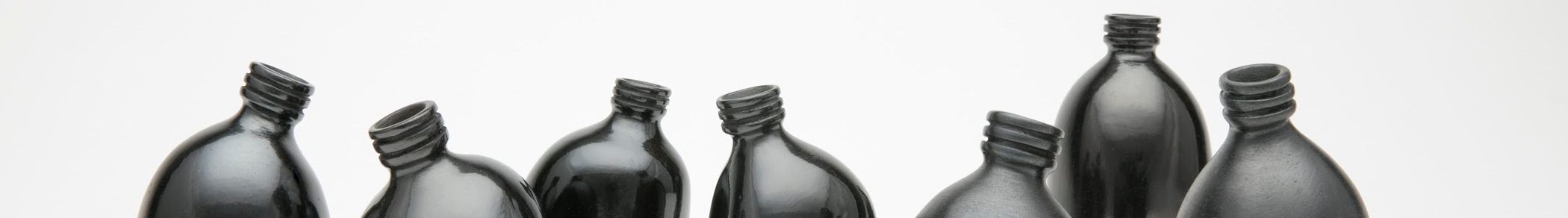 Against a stark white background are seven small clay vessels painted a dark, shiny black. They look like miniature plastic water bottles and are each slightly bent, making them appear like a gathering of people interacting.