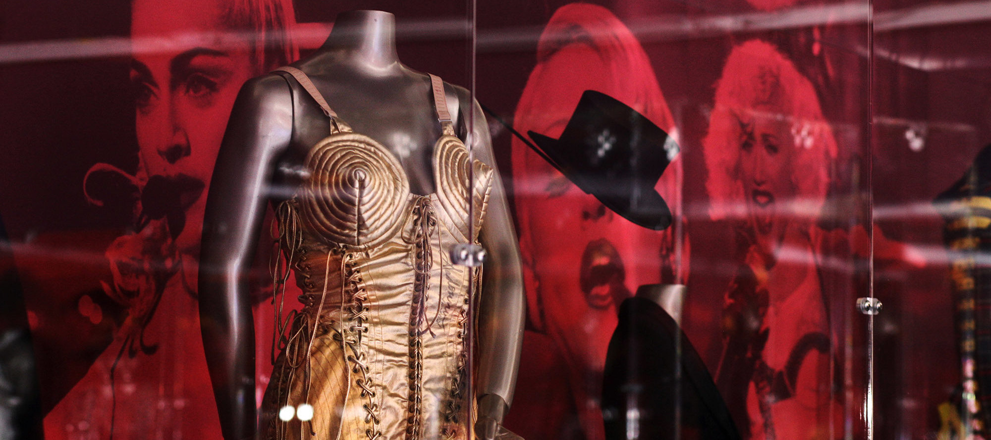 Display case showing an iconic outfit worn by Madonna, a gold thin strapped dress with conical breasts.