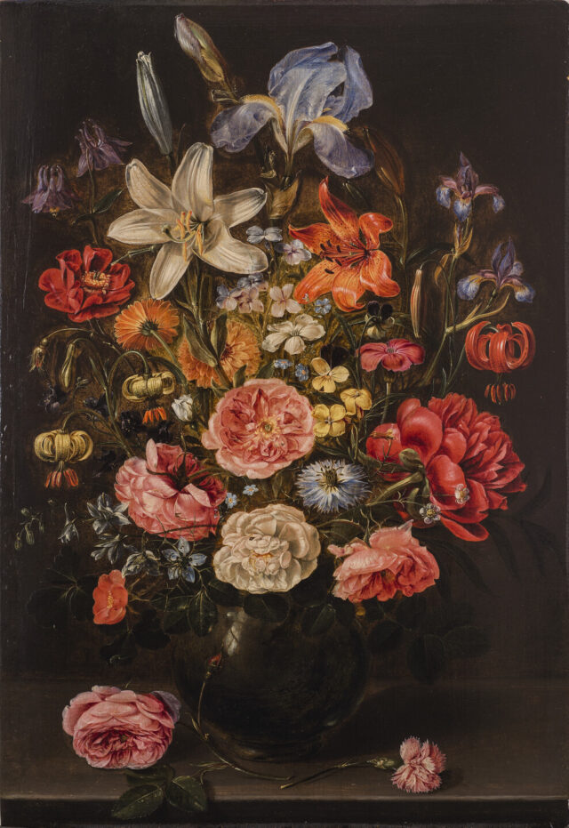 Realistic and detailed, a dramatic still-life painting features a large arrangement of varied, brightly colored flowers in a dark, round vase against a dark background. The vase sits on a stone ledge with two stray pink roses lying in the foreground.