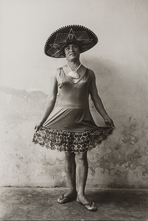 A black-and-white portrait photograph of a woman wearing a sombrero and a traditional Mexican dress, smiling at the camera.