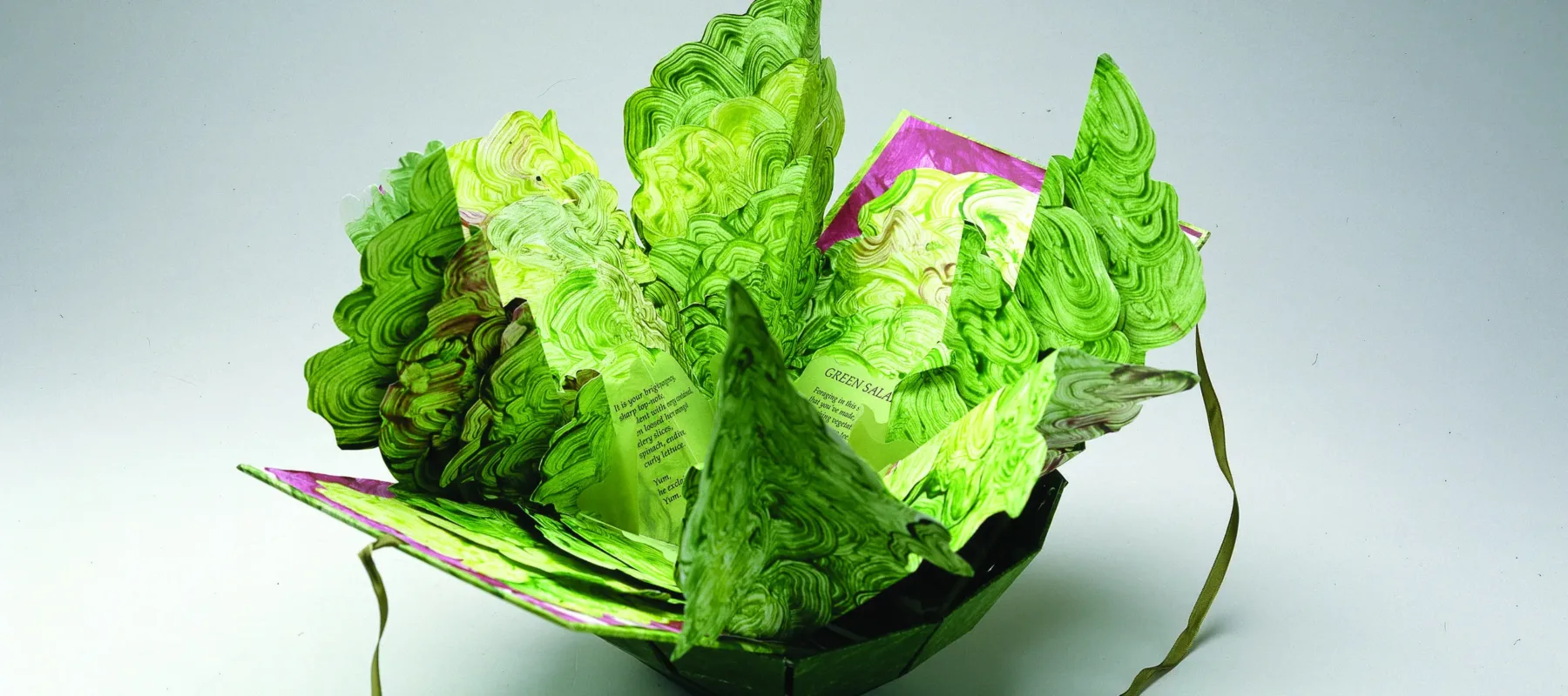 Artist's book resembling a salad in a bowl. Constructed of Tyvek that has been painted in swirling greens and map-folded to look like leaves of lettuce, there is poem written on the inner the leaves.