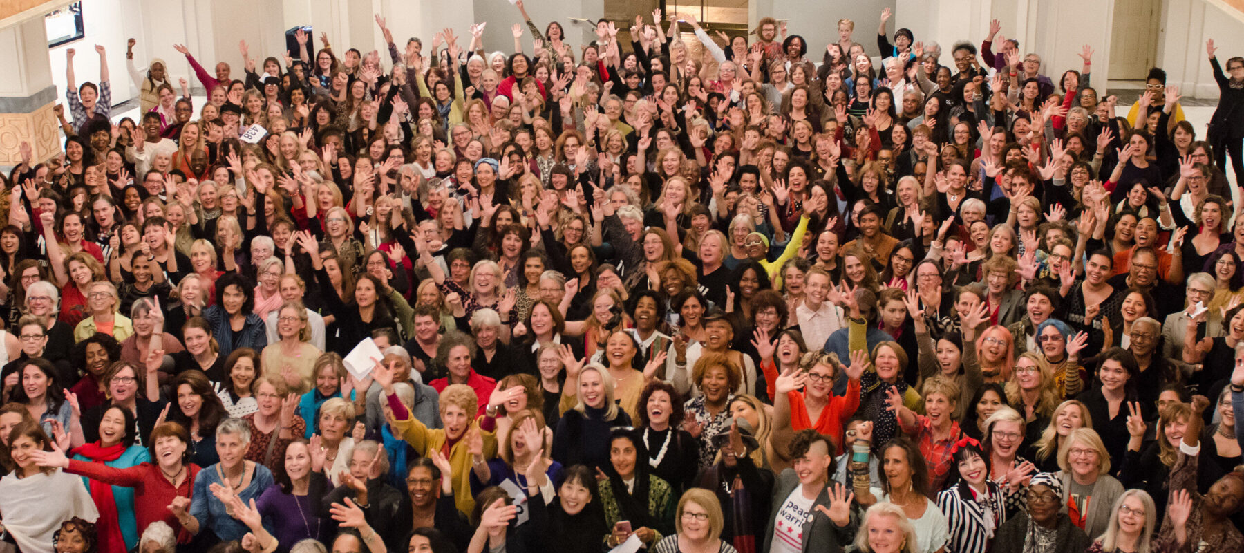 A color photograph of 435 women from a high vantage point. The women all look up towards the camera, some with arms outstretched.
