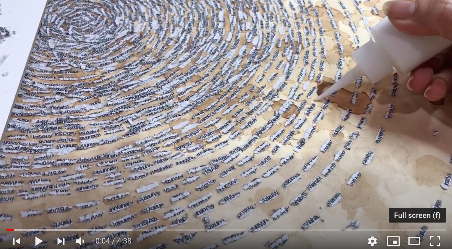 Still frame from a video of Ambreen Butt's hand delicately applying glue to paper to affix cutout words