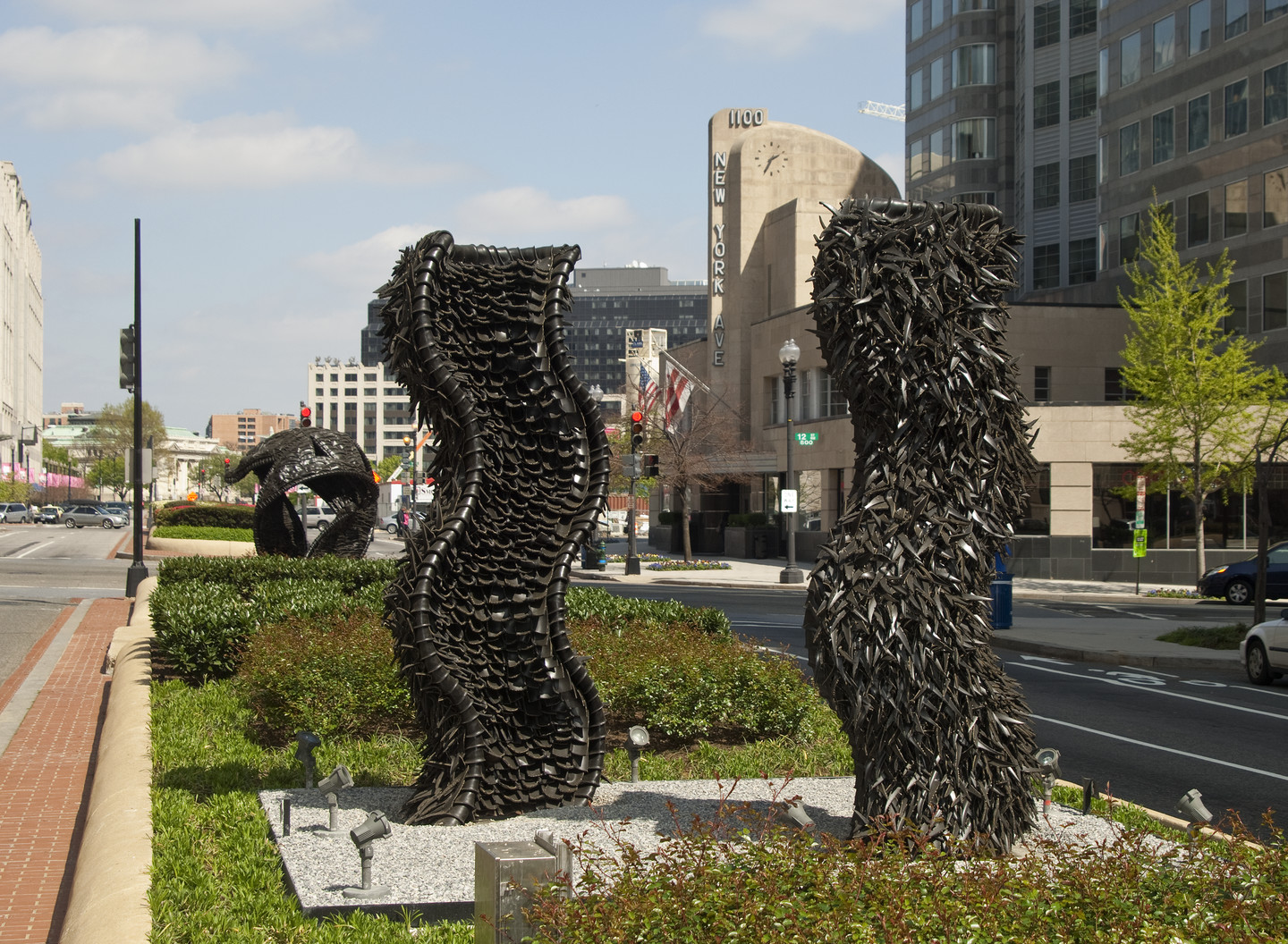 Two large abstract sculptures made from tires rise from a center median in a city street. The sculptures are wavy columns.
