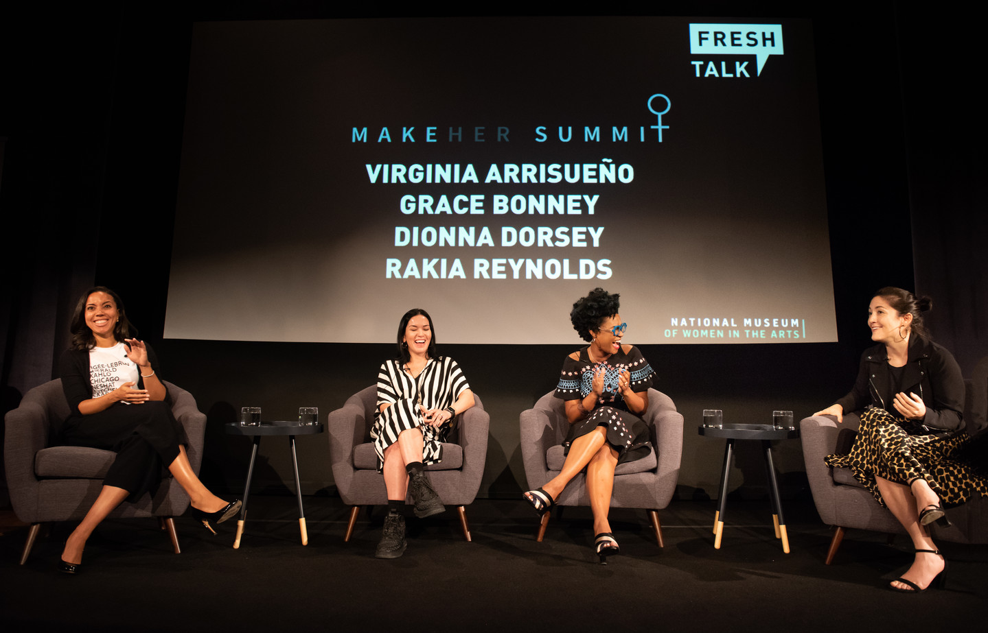 Four women sit in armchairs on a stage. They are engaged in a lively conversation. Behind them a projection reads “MakeHer Summit: Virginia Arrisueño, Grace Bonney, Dionna Dorsey, Rakia Reynolds.” There is a Fresh Talk logo in the top corner of the screen and a National Museum of Women in the Arts logo in the bottom corner.
