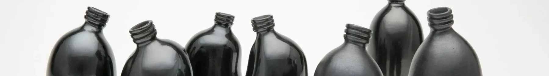 Against a stark white background are seven small clay vessels painted a dark, shiny black. They look like miniature plastic water bottles and are each slightly bent, making them appear like a gathering of people interacting.