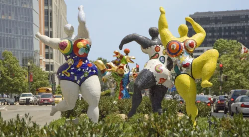 Three abstract outdoor sculptures of voluptuous figures covered in bright patterns and dancing with outstretched arms.