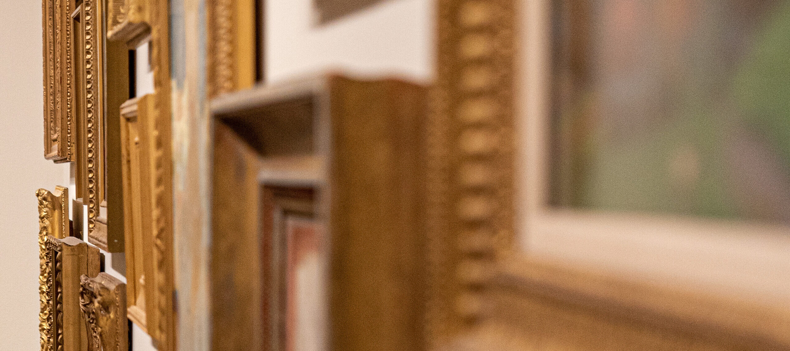 Close up shot of a gallery wall installed salon style, with many small paintings hung closely together.