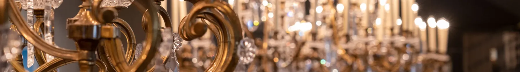 Close-up view of ornate gold and crystal chandeliers in the museum's Great Hall. The camera is focused on the chandelier in the foreground and the rest is out of focus.