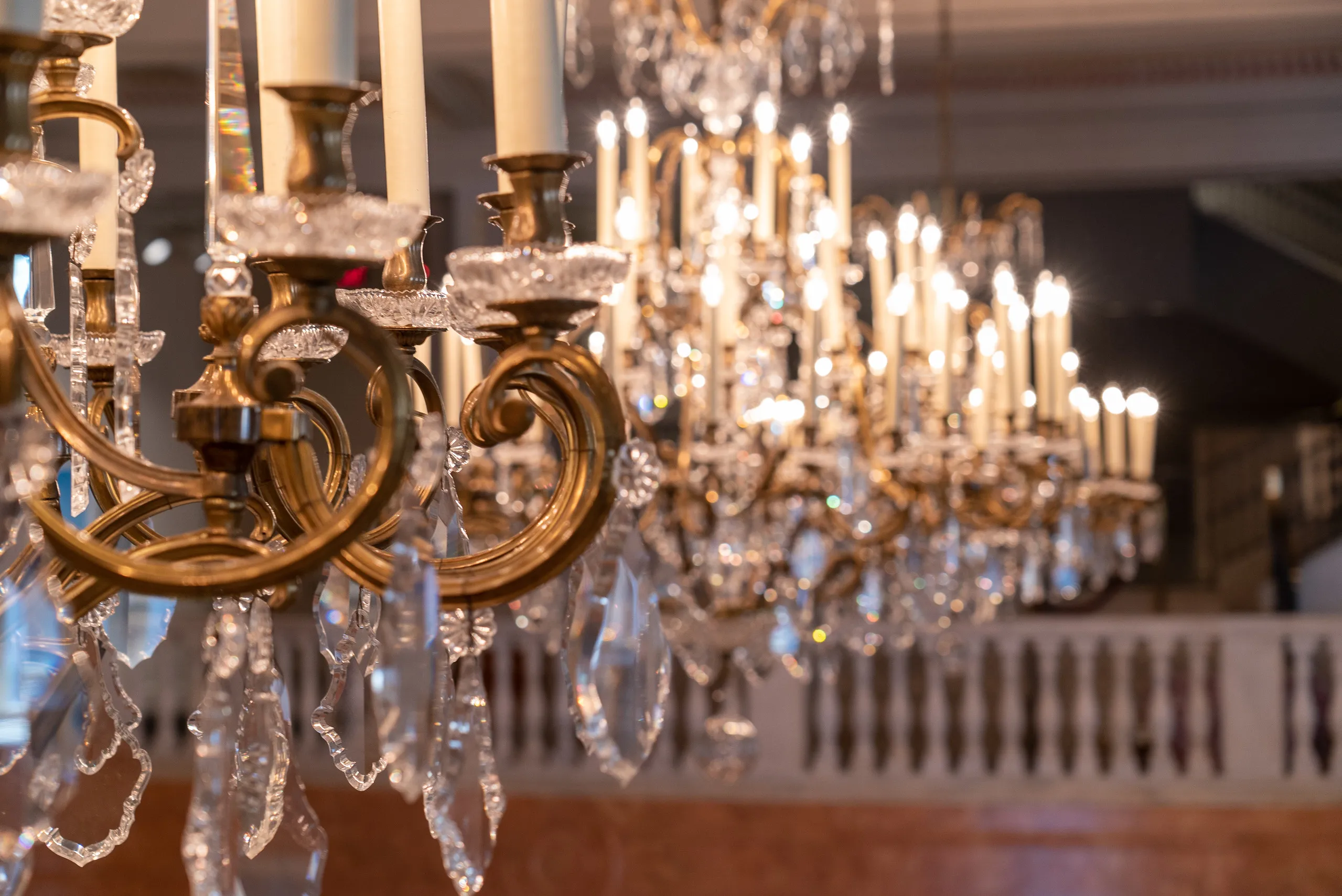 Close-up view of ornate gold and crystal chandeliers in the museum's Great Hall. The camera is focused on the chandelier in the foreground and the rest is out of focus.