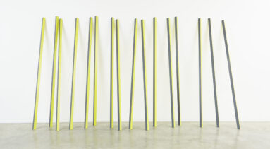 Sixteen rectangular yellow and grey aluminum poles lean up against a wall