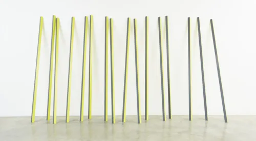 Sixteen rectangular yellow and grey aluminum poles lean up against a wall