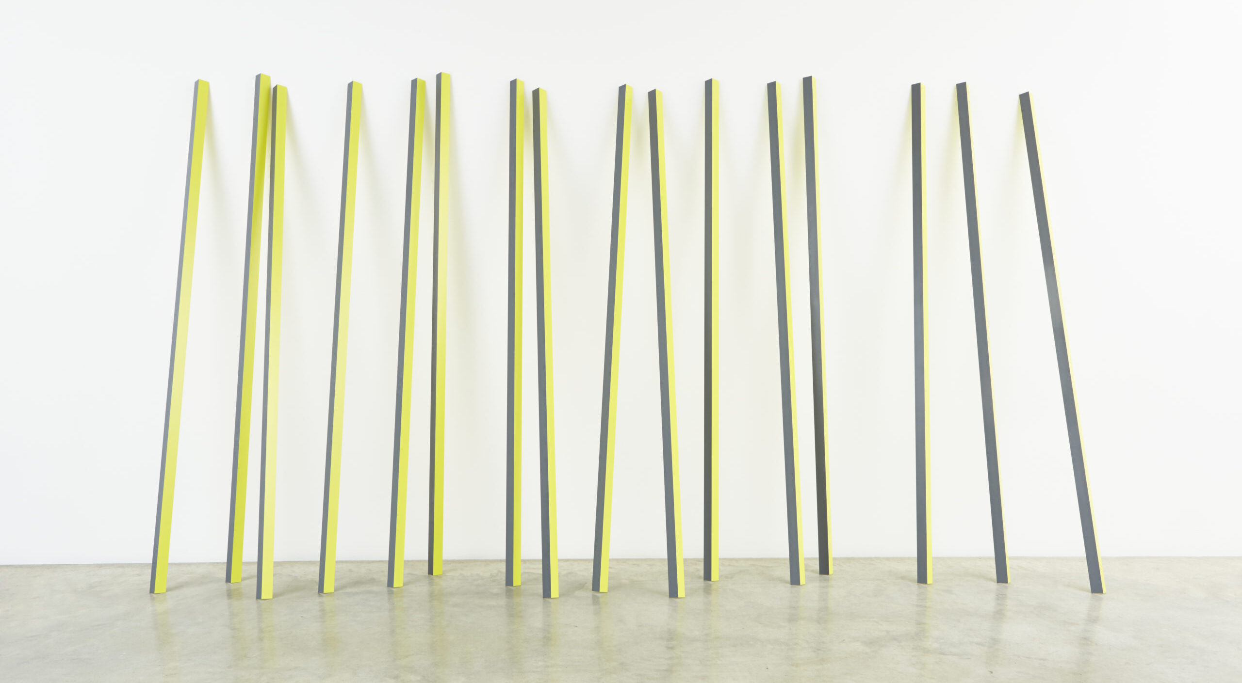 Sixteen rectangular yellow and grey aluminum poles lean up against a wall