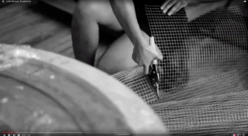 Black and white still image from a video on Leila Khoury shows the artist cutting chicken wire with clippers.