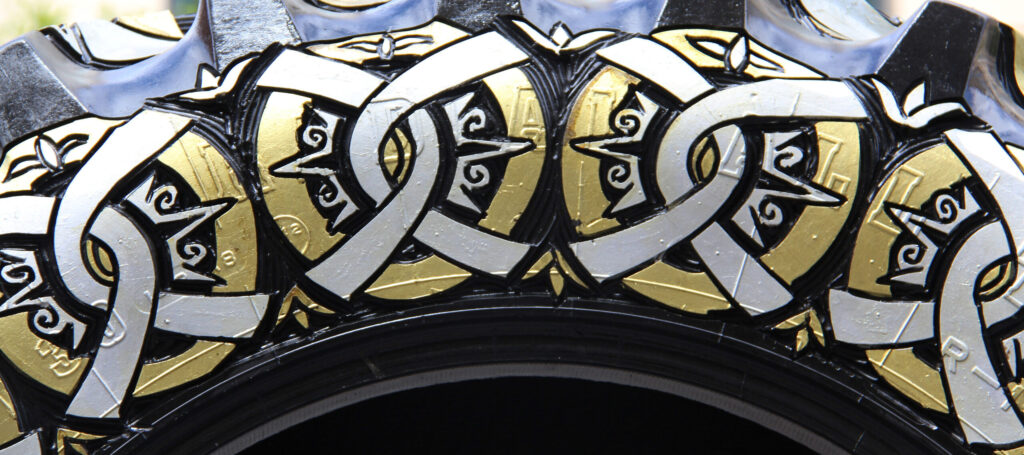 Close-up photograph of a sculpture made of a truck tire carved with circular designs and painted gold and silver