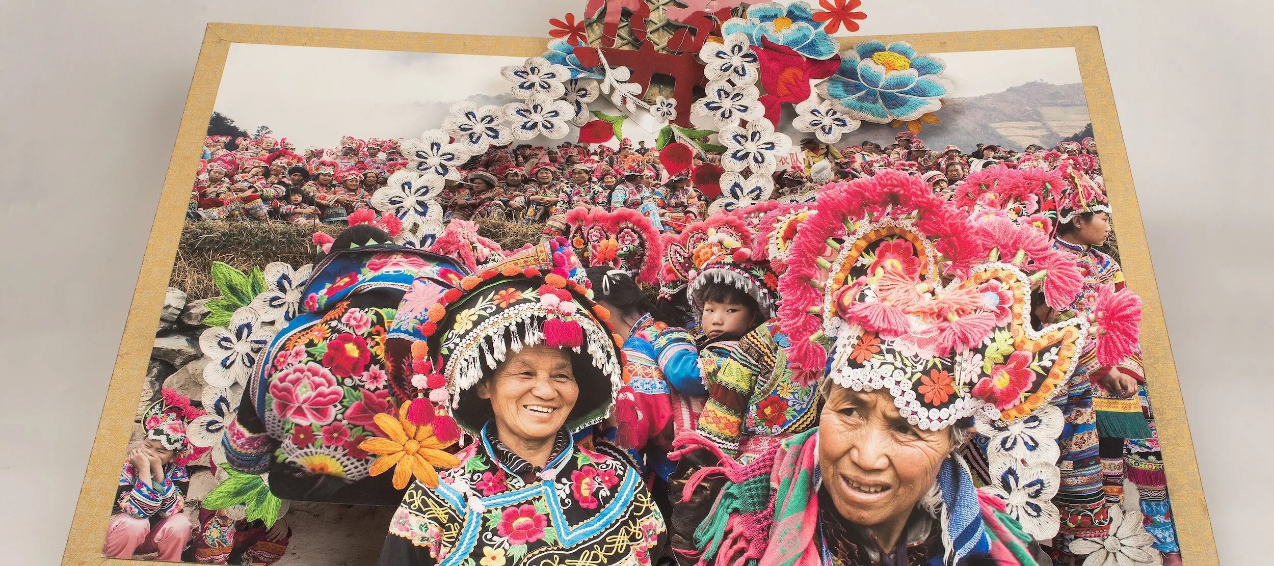 Large-scale pop-up book depicts the culture and traditions minority areas in China by showing numerous people in brightly colored, traditional dress.