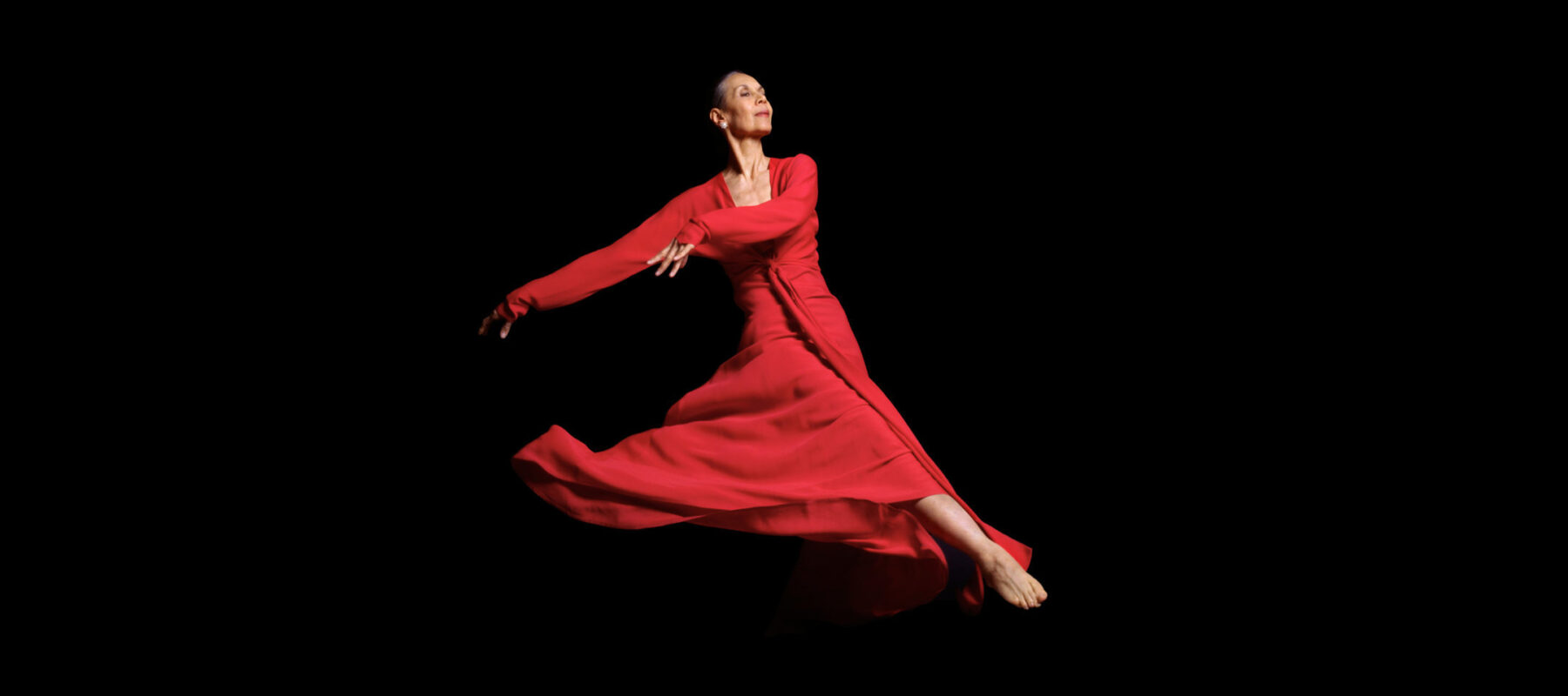 An older woman dances in a flowing red dress, appearing as if she's floating through space. Her face is turned to the right and she wears an expression of calm and fulfillment.