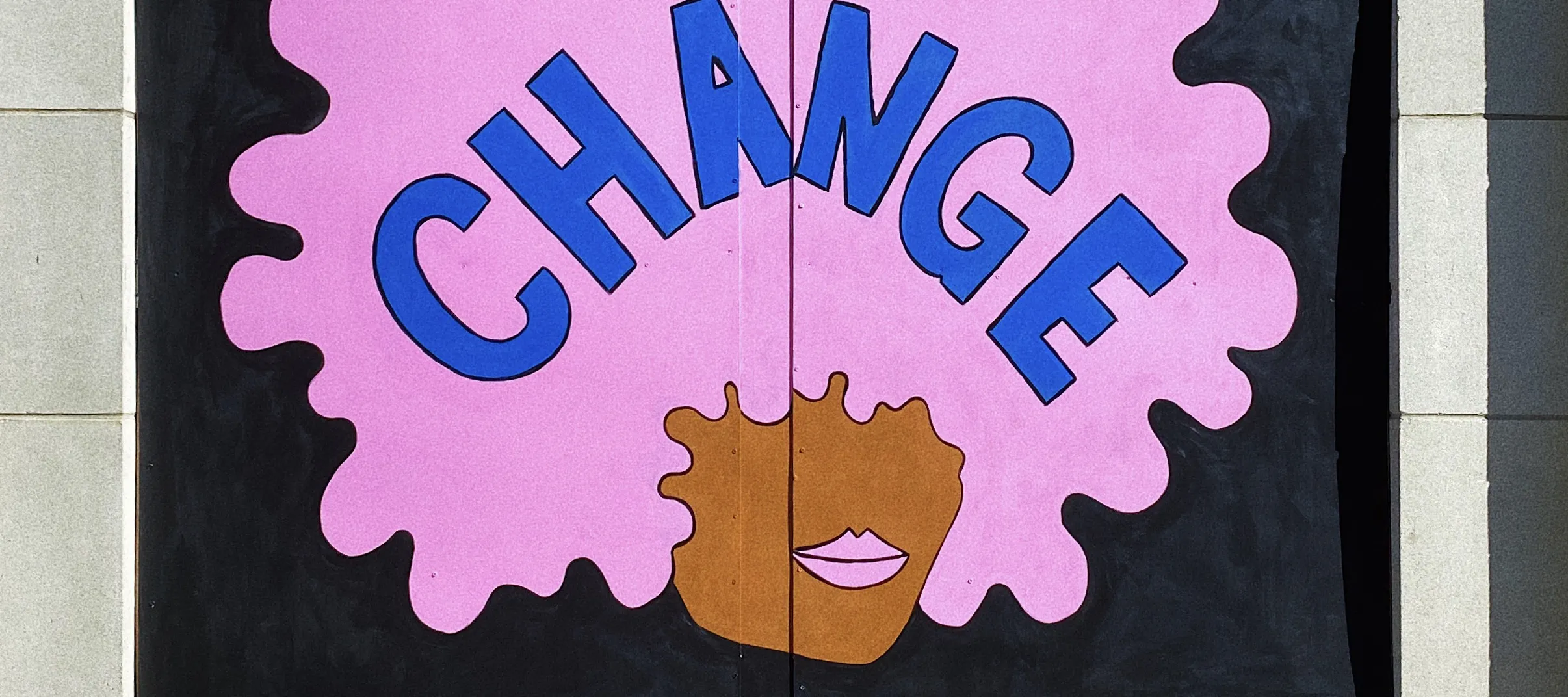 A plywood mural of a dark-skinned face with a bubblegum pink afro and matching, full lips, against a black background. "CHANGE" is written in blue letters across the afro.