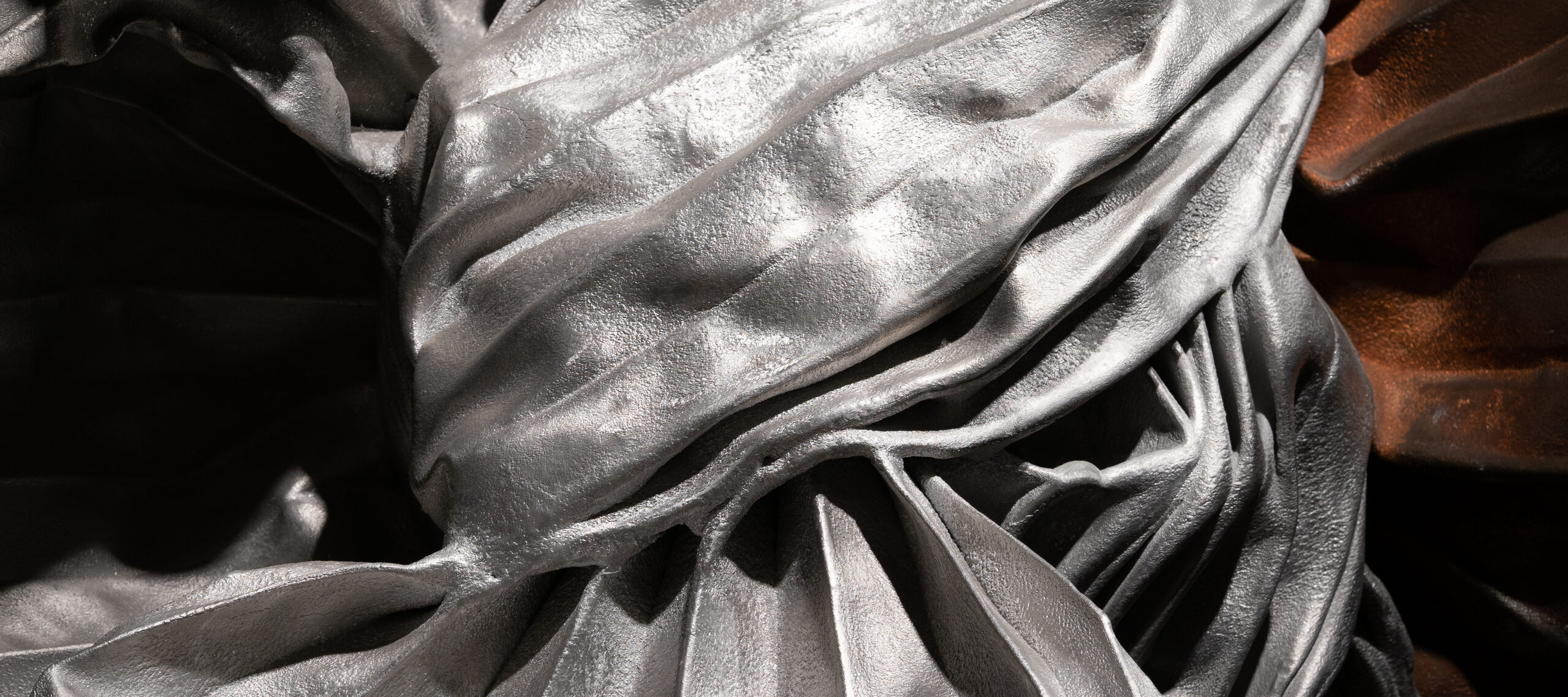 A close-up of a silver, metal sculpture that appears to be tied in a giant knot with crisp folds in the metal sheets.