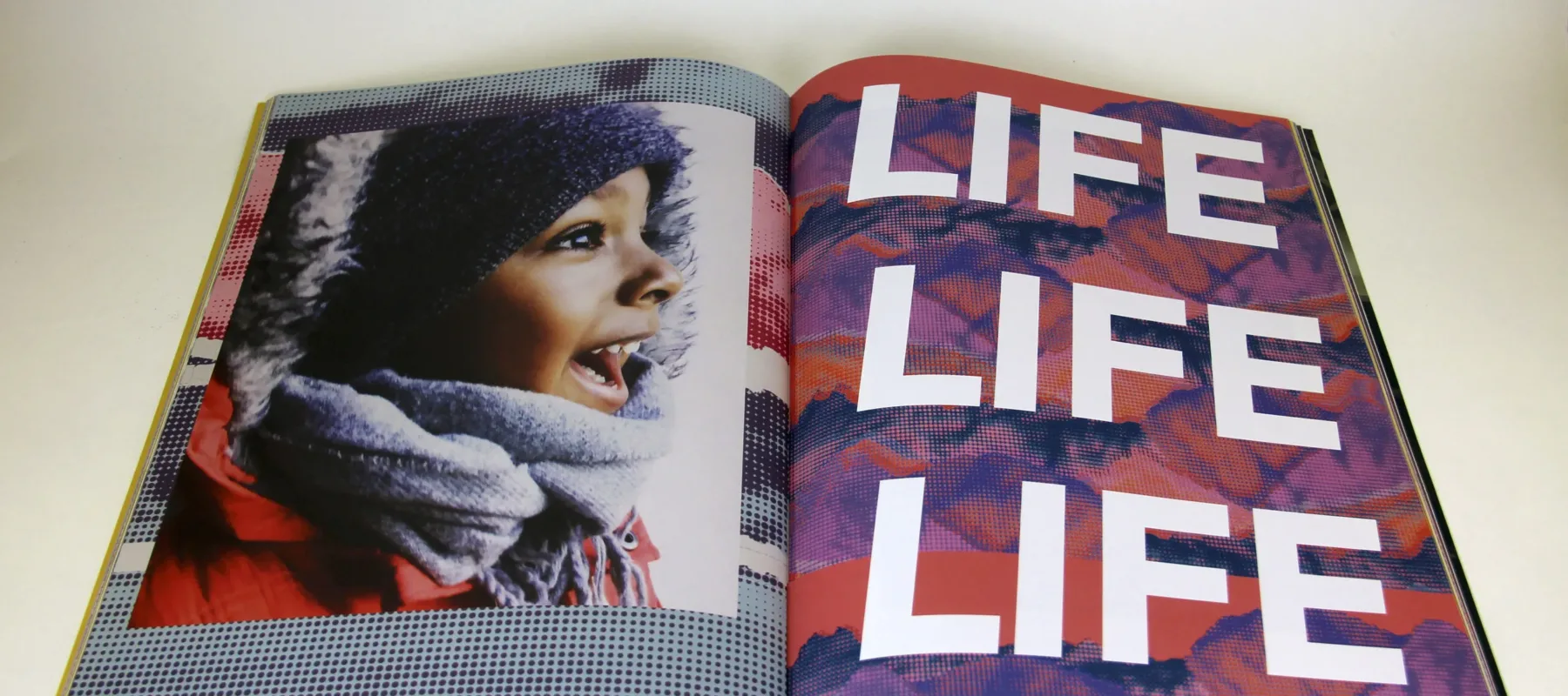 Open book features photograph of a child with medium-brown skin on the left side of the fold and the words "LIFE LIFE LIFE" filling the page on the right.