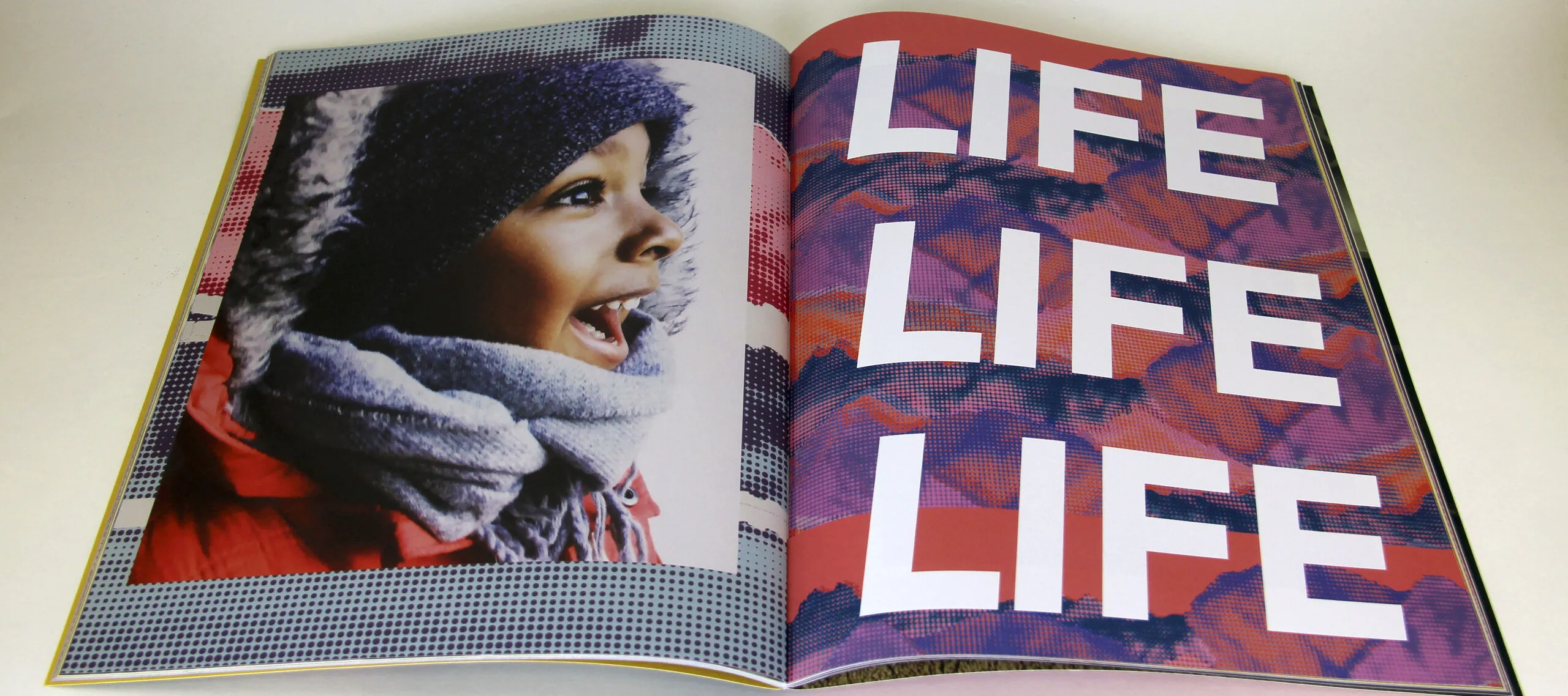 Open book features photograph of a child with medium-brown skin on the left side of the fold and the words "LIFE LIFE LIFE" filling the page on the right.