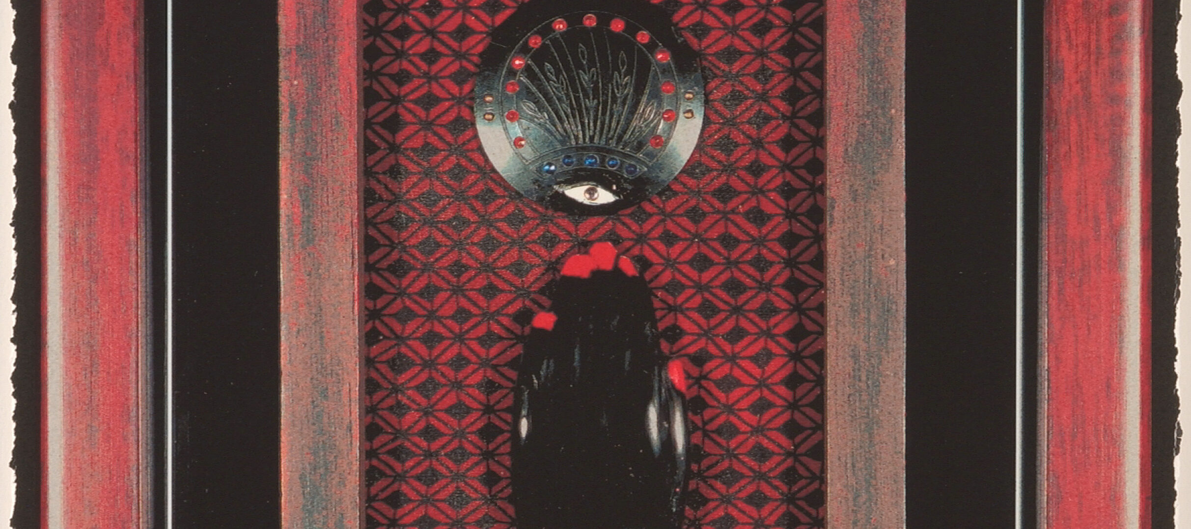 A black left hand with bright red nails and a red bracelet in a red wooden frame. It sits atop a black and red patterned background, fingers pointing toward a black medallion with an eye and other details. The red frame is surrounded by black and sits within a larger red frame.