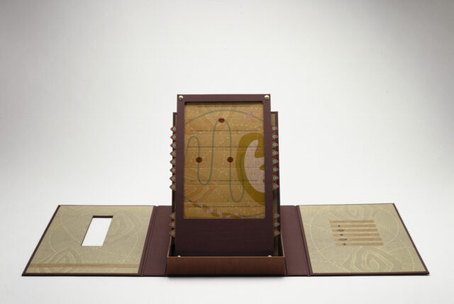 An open maroon portfolio with contents displayed upright in center. Upright panel is an abstract image with red circles connected by a curving green line on a mustard yellow background.