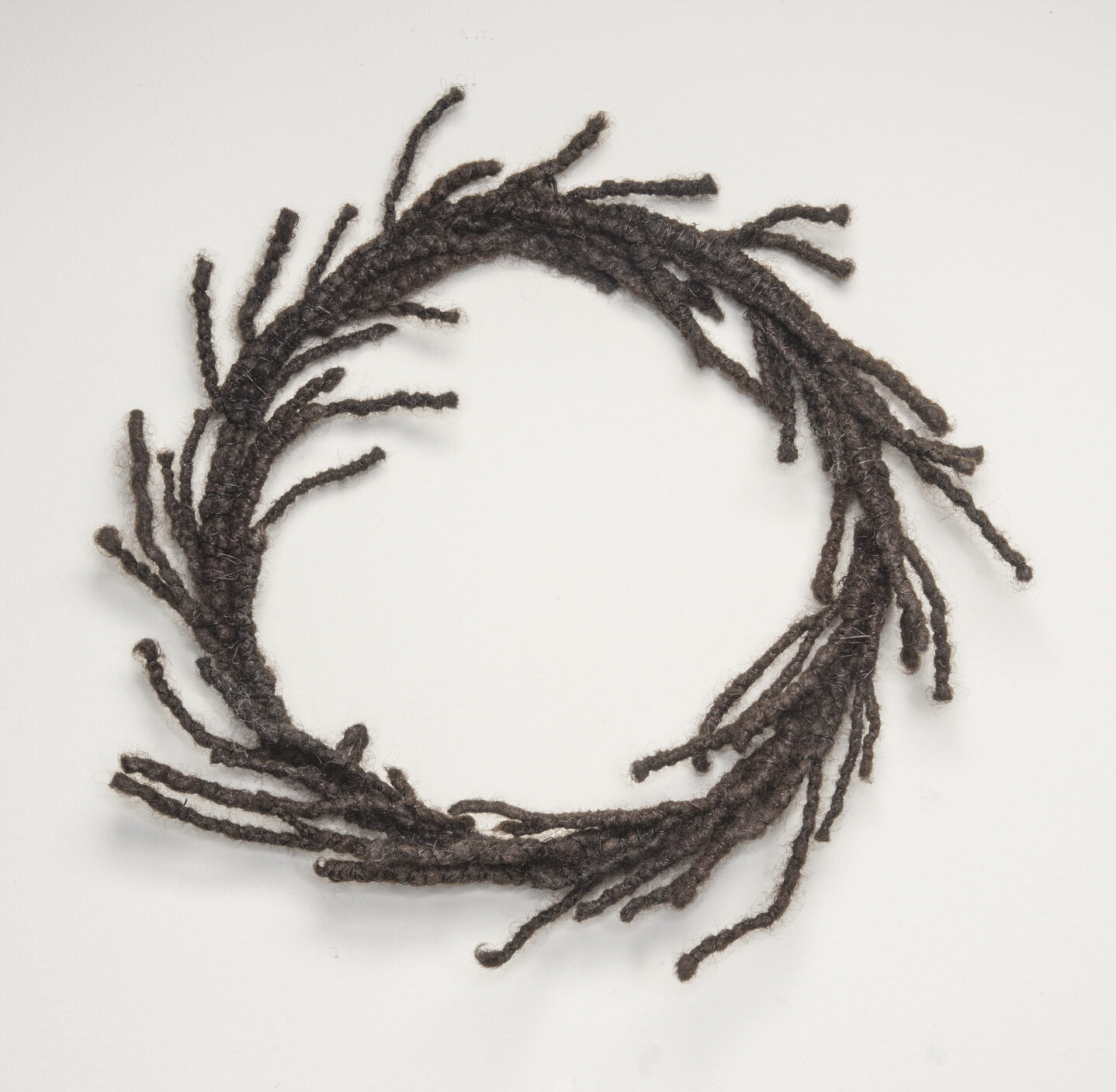 A circular wreath made of dark, tightly coiled hair with strands escaping and resembling laurels.