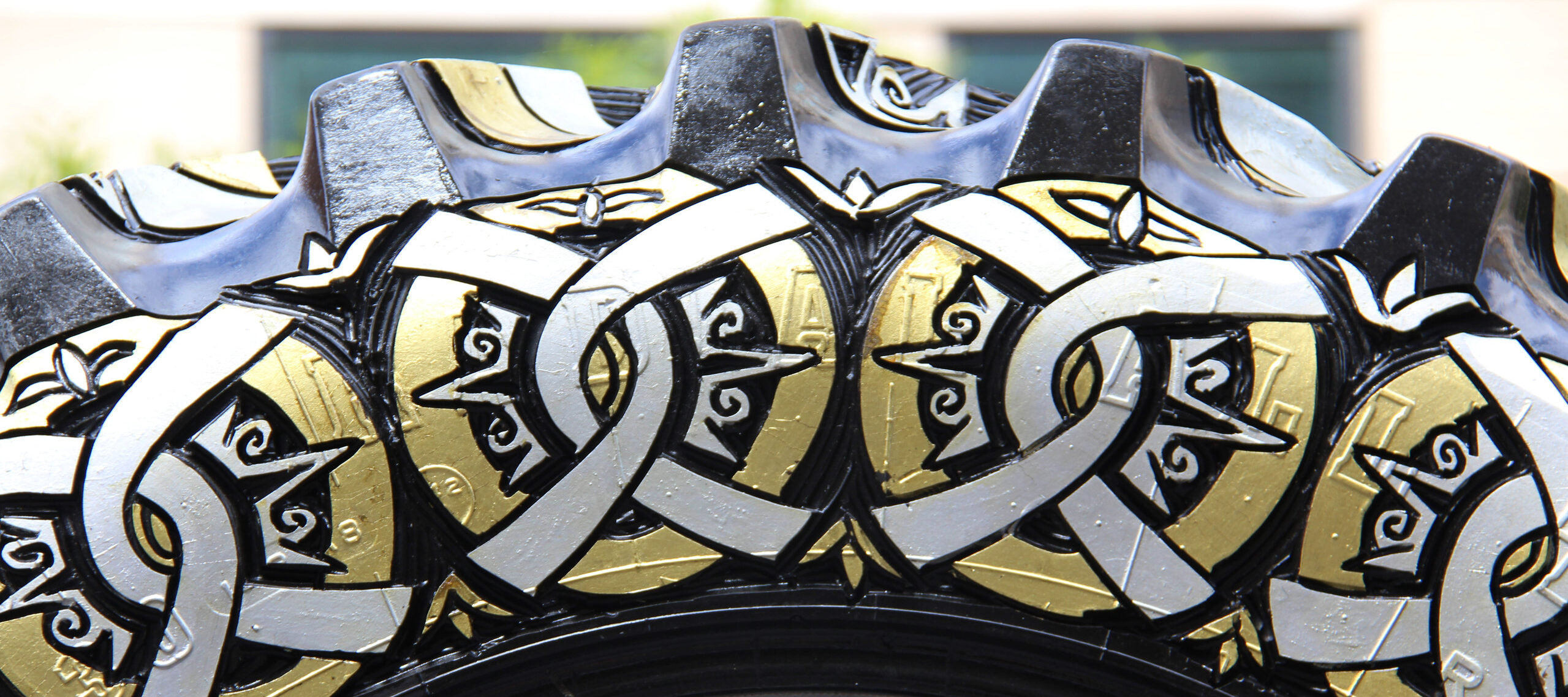 Close up view of an oversized tire with carved designs painted in silver and gold.