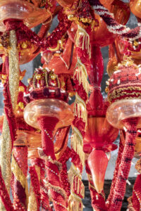 A color image of a detail of a chandelier made of red, orange, and yellow Murano glass, wool yarn, polyester fabrics, and LED lighting.