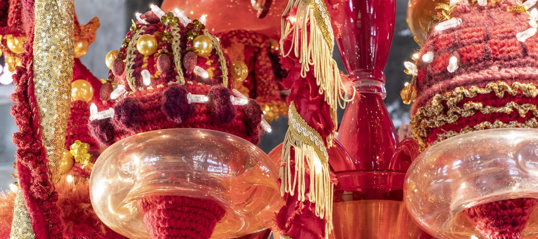 A color image of a detail of a chandelier made of red, orange, and yellow Murano glass, wool yarn, polyester fabrics, and LED lighting.