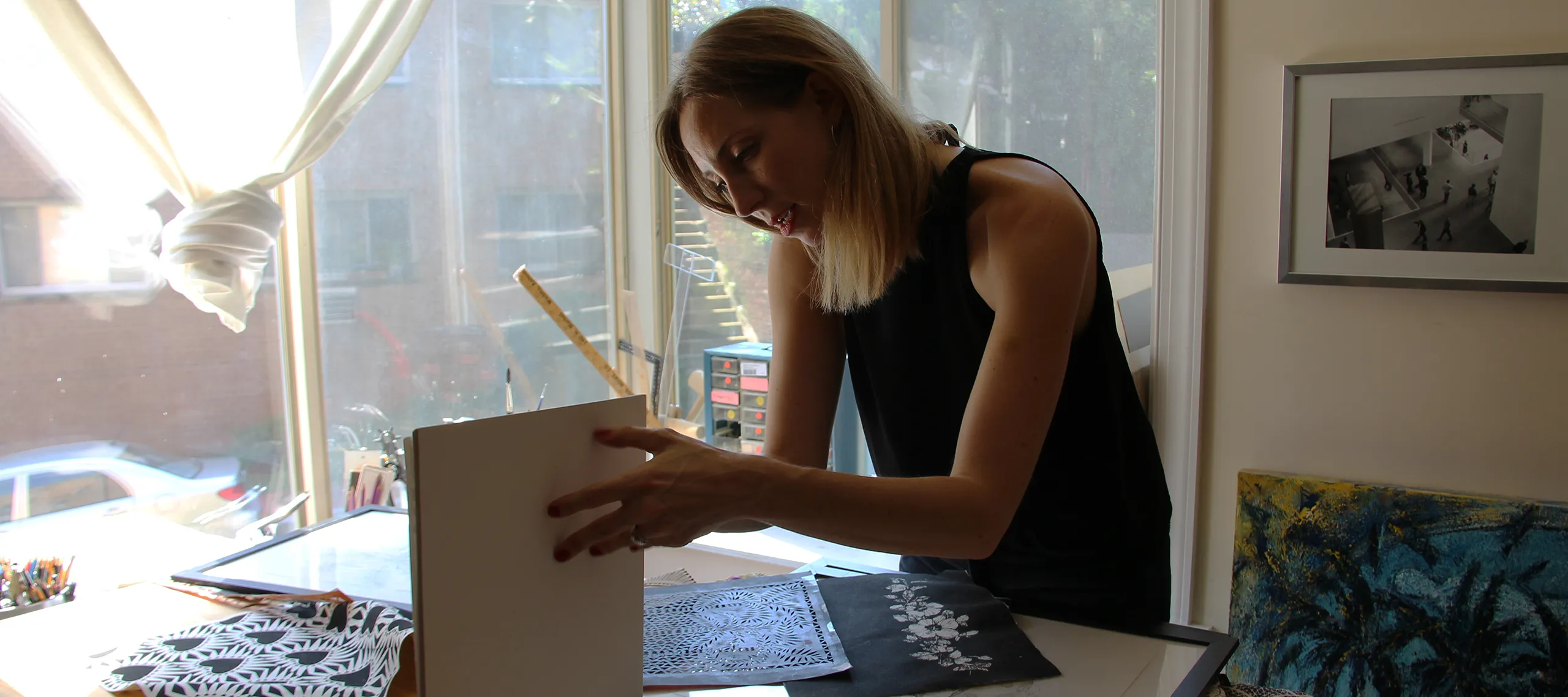 A woman in her home. She has a light skin tone and blonde hair, and is in the midst of flipping a book open.