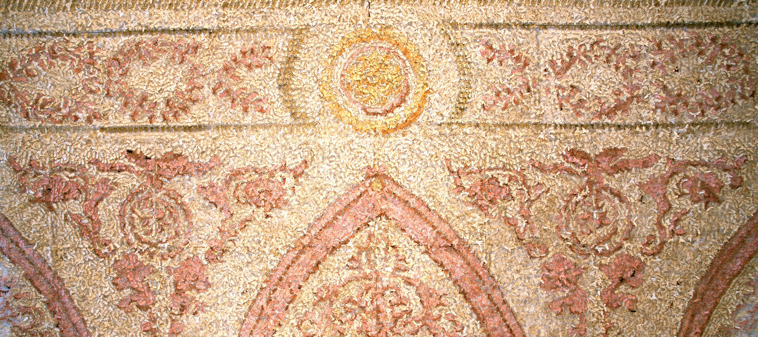 A colored image of what appears to be a wall decorated with mosaics in red and yellow tones. Upon closer inspection each shape is actually an origami bug.