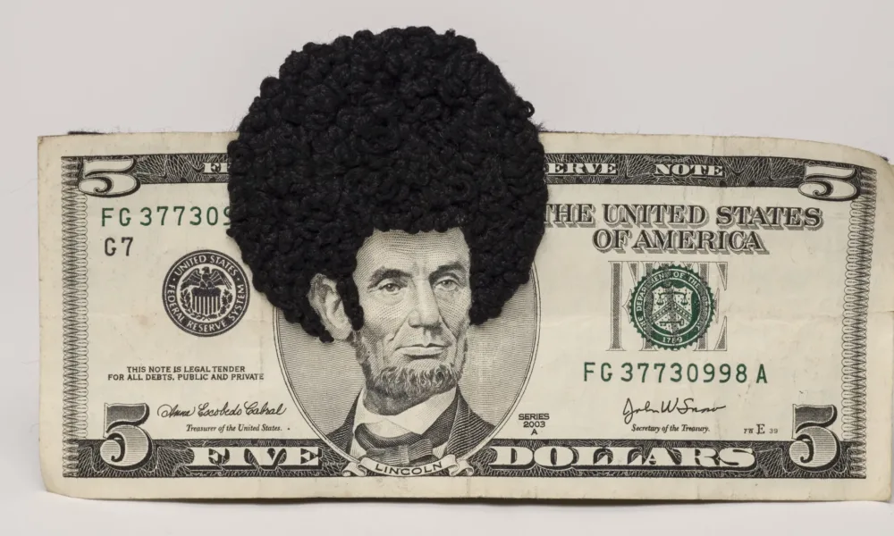 U.S. five-dollar bill has an embroidered afro and sideburns stitched onto the portrait of Lincoln’s head. One-third of the afro protrudes beyond the top of the bill.