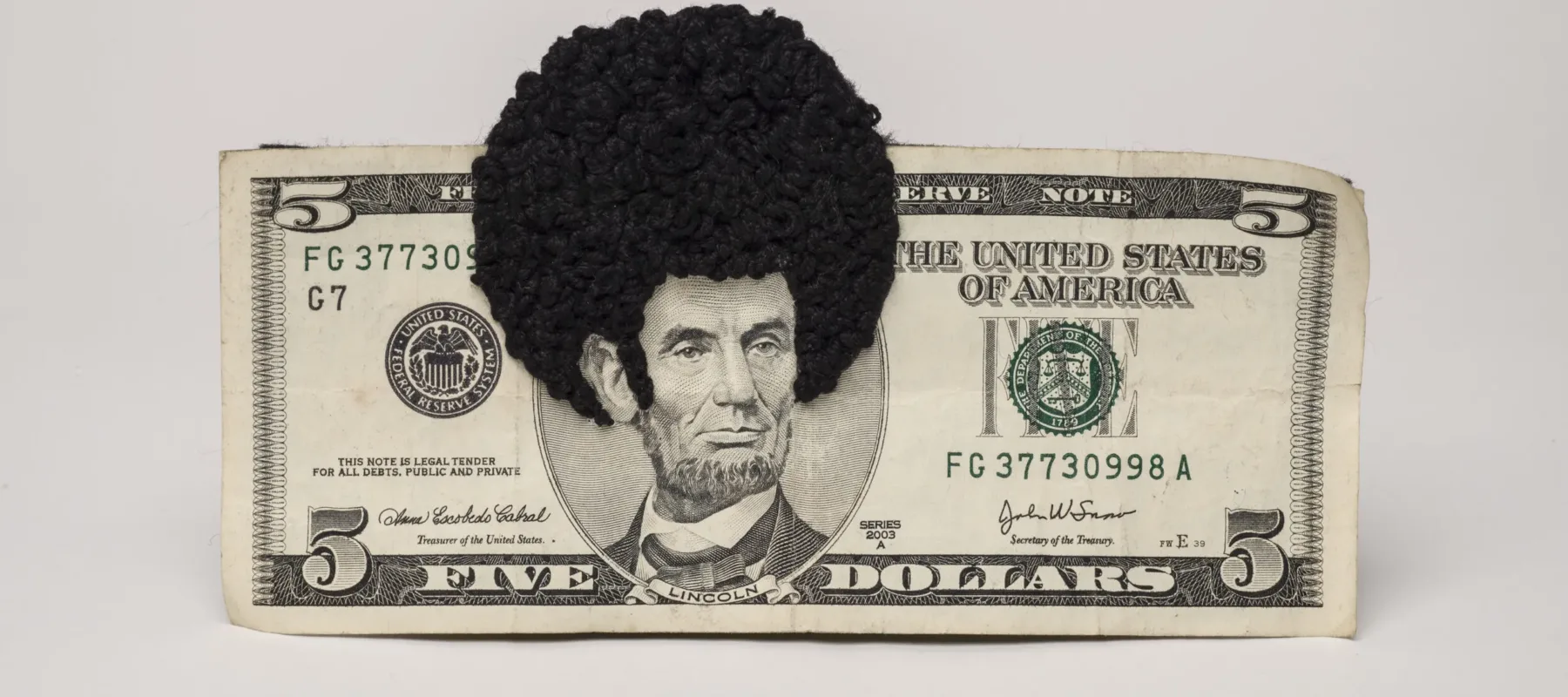 U.S. five-dollar bill has an embroidered afro and sideburns stitched onto the portrait of Lincoln’s head. One-third of the afro protrudes beyond the top of the bill.