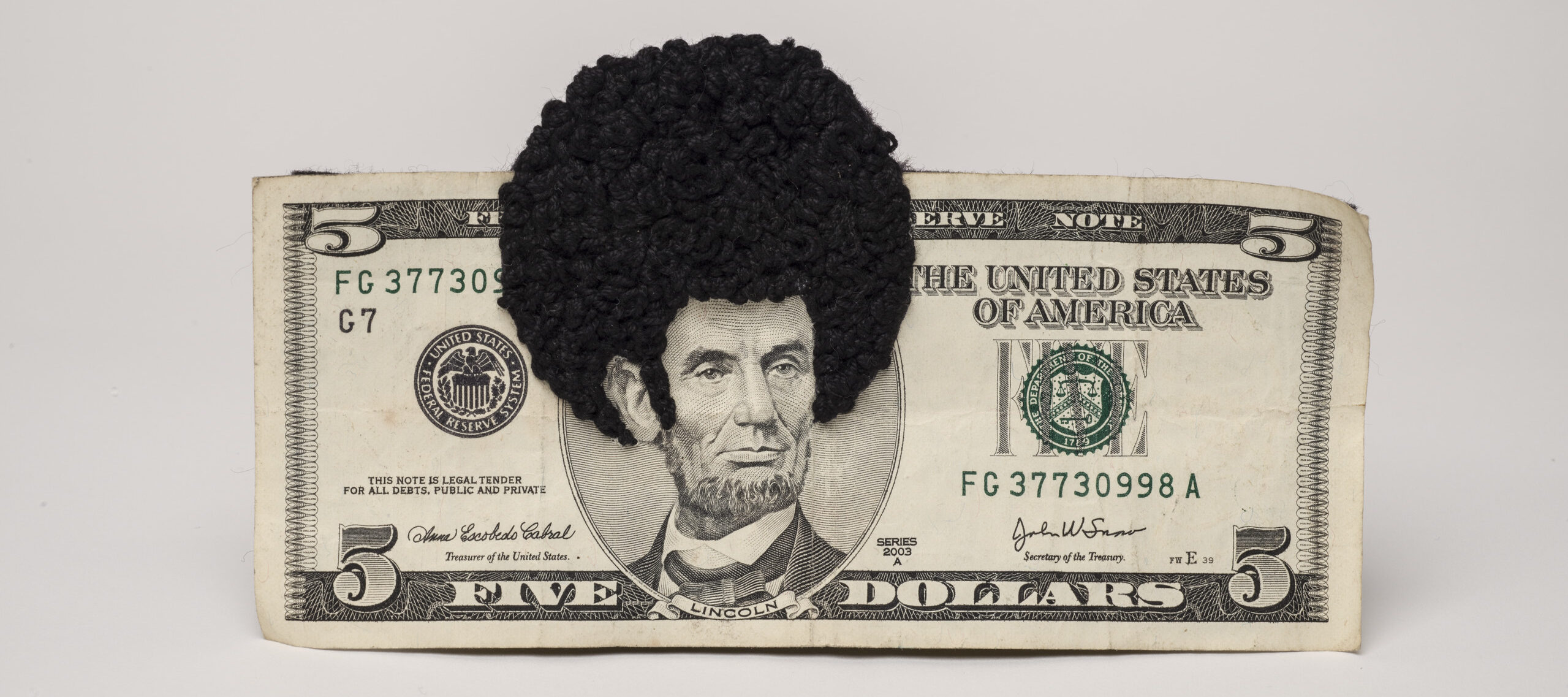 U.S. five-dollar bill has an embroidered afro and sideburns stitched onto the portrait of Lincoln’s head. One-third of the afro protrudes beyond the top of the bill.
