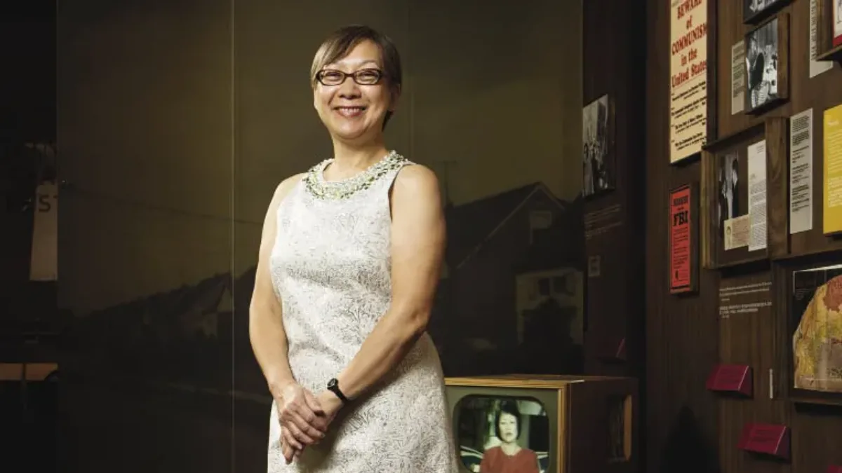 A light-skinned Asian woman stands smiling in front of a historical exhibition showcasing posters and a TV from the 1950s.